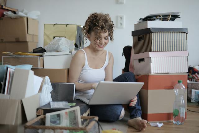 Woman using her laptop on the floor, surrounded by lots of boxes and clutter