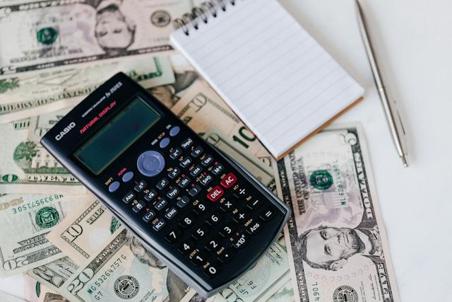 A calculator, a pen, and a notepad on a pile of money